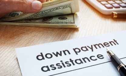 Hand Sorting Money Next To A Paper Stating Down Payment Assistance